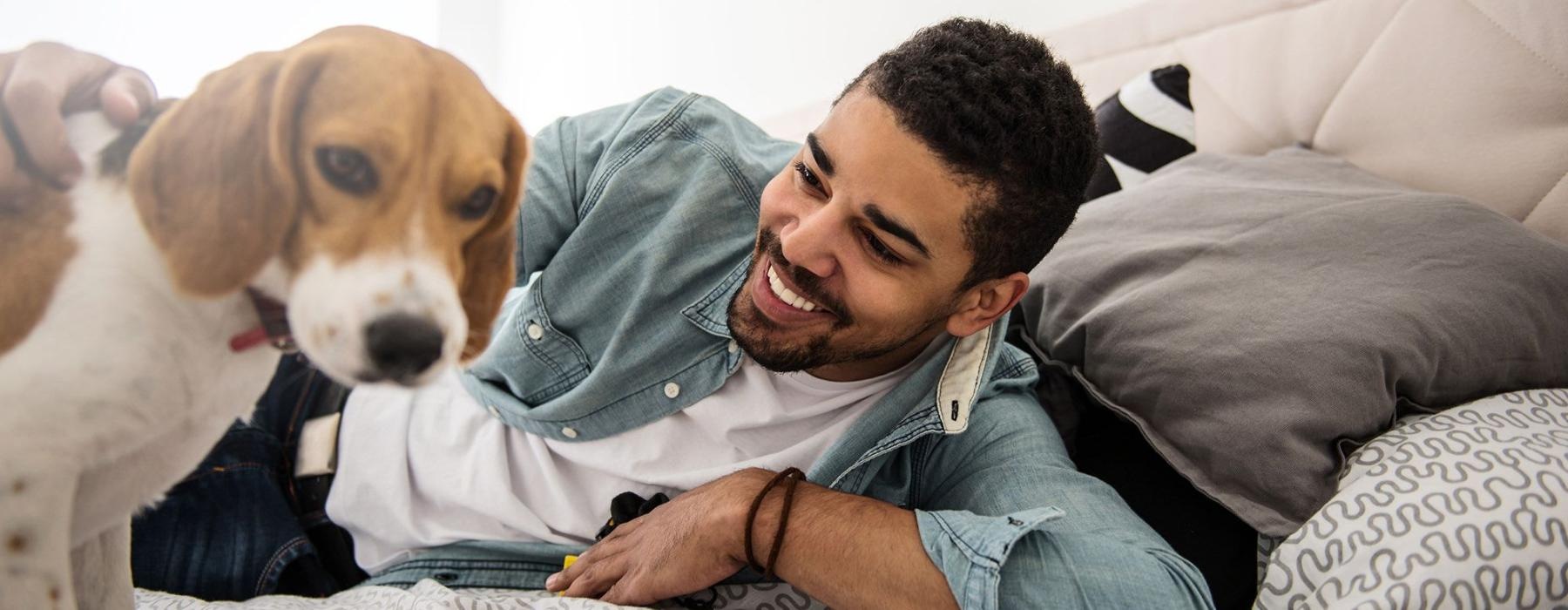 man smiles and pets his dog on a bed